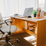 A modern office workspace featuring a wooden desk, office chair, laptop, and bright natural light.