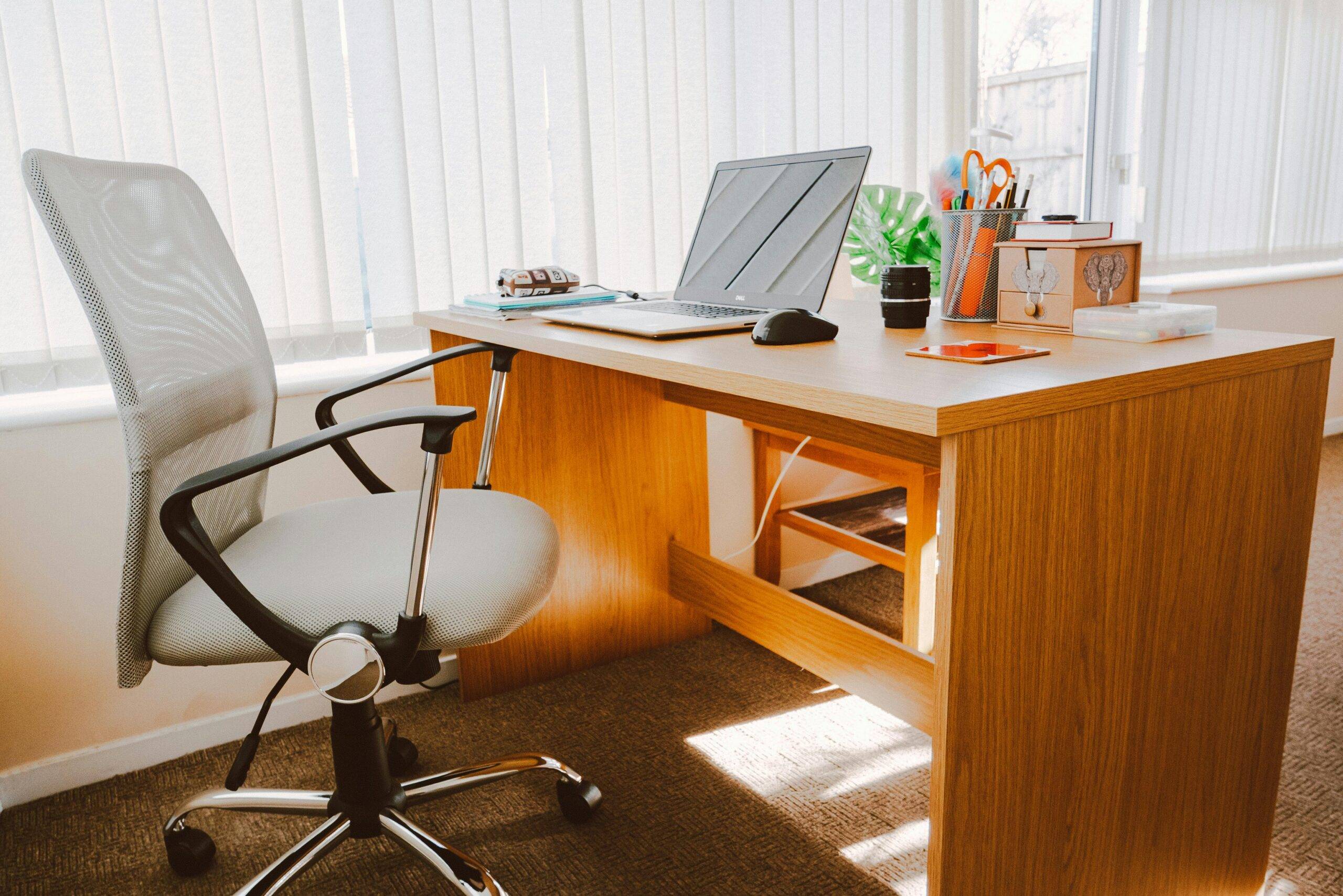 A modern office workspace featuring a wooden desk, office chair, laptop, and bright natural light.