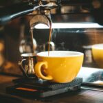 Coffee Maker steaming espresso pours into a yellow cup in a cozy café.