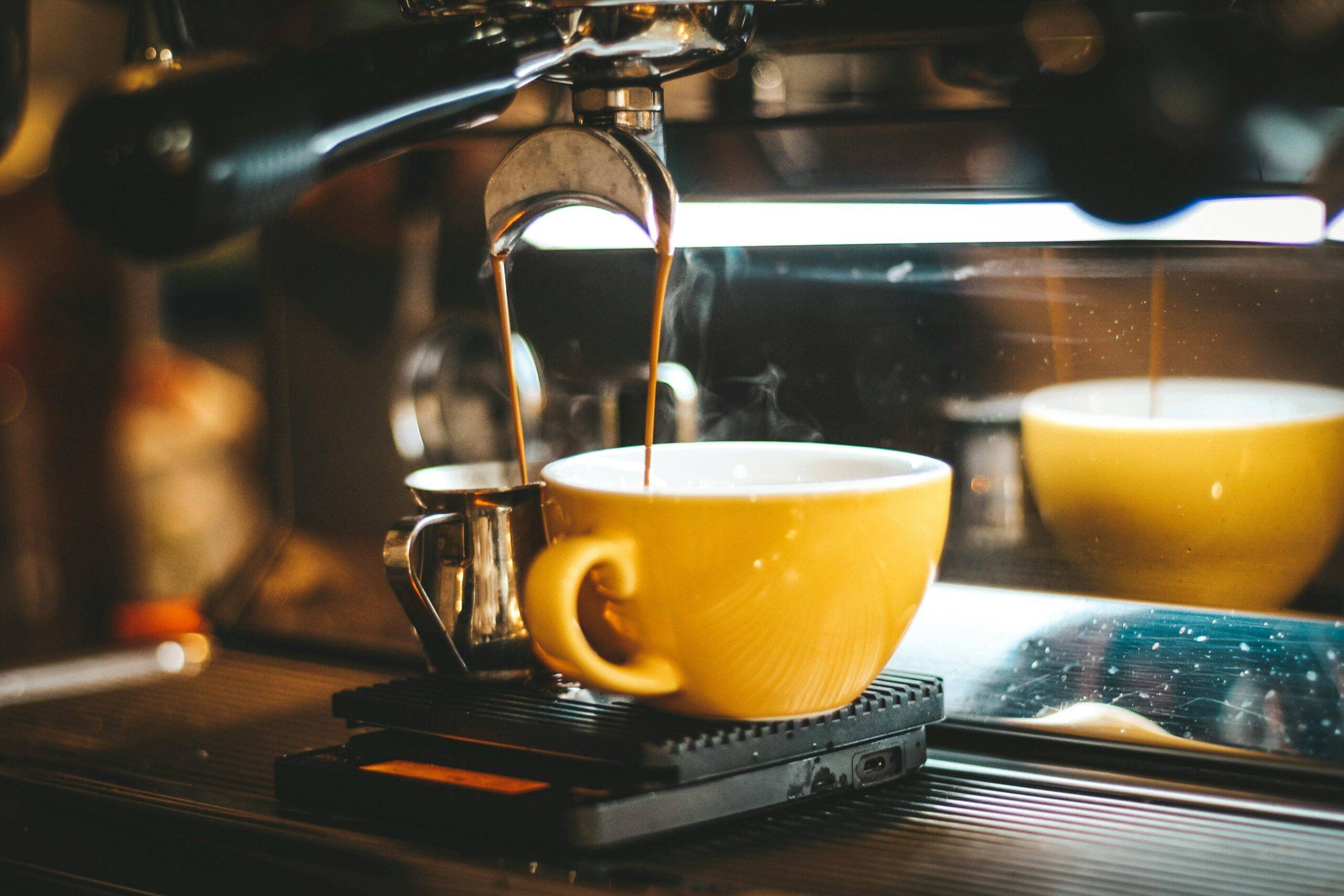 Coffee Maker steaming espresso pours into a yellow cup in a cozy café.