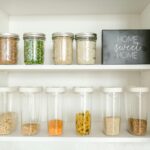 Neatly arranged glass and plastic jars containing grains and pasta in a kitchen cabinet.